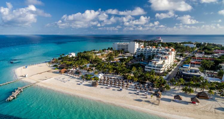 Vue aérienne d'un complexe tropical au bord de la plage avec des eaux turquoise.