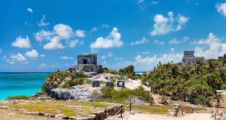 Ruins of a Mayan temple overlooking a turquoise sea, surrounded by lush vegetation.