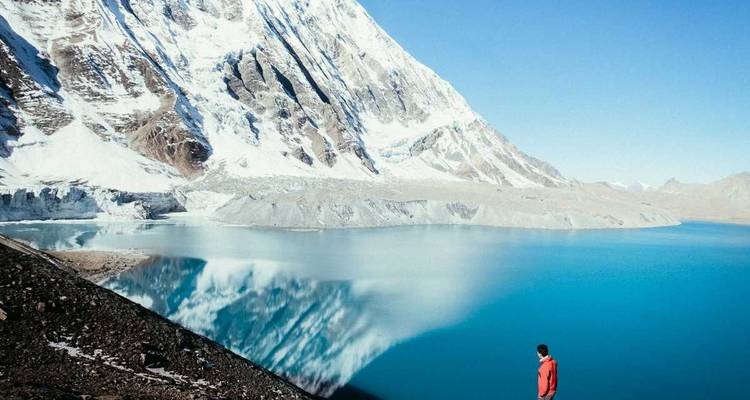Person in red jacket overlooking a blue lake and snowy mountains.