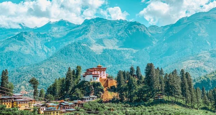 Scenic view of a traditional Bhutanese building on a hill with mountains.