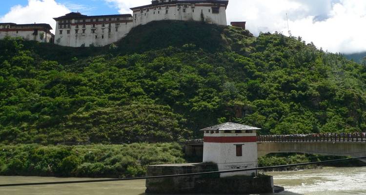 Bhutanese building on a green hill near a river.