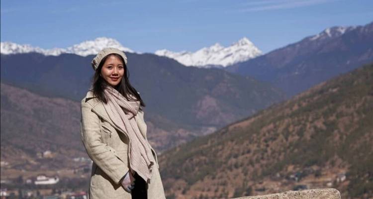 Persona posando con montañas cubiertas de nieve en el fondo.