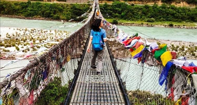 Person, die auf einer Hängebrücke mit Gebetsfahnen geht
