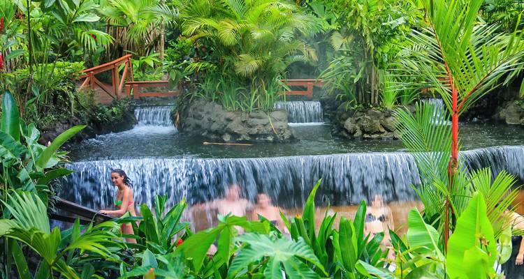 Personas disfrutando de una fuente termal tropical con cascadas.