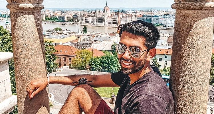 A traveller sits between stone columns overlooking Budapest’s Parliament and the Danube.