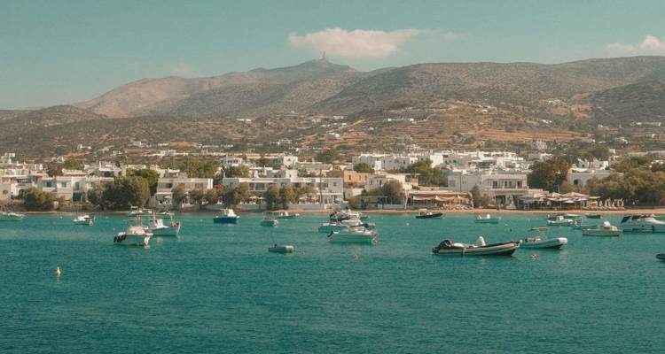 Griechisches Küstendorf mit weißen Häusern und Booten, die in einer ruhigen, türkisfarbenen Bucht ankern.