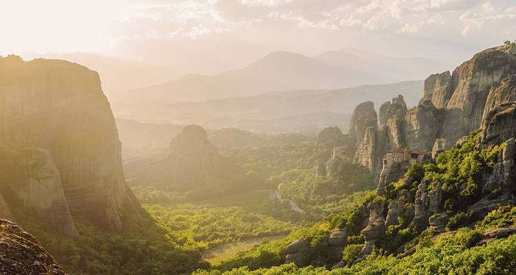 Falaises dorées par le soleil et monastères des Météores s'élevant au-dessus d'une vallée verdoyante à l'heure dorée
