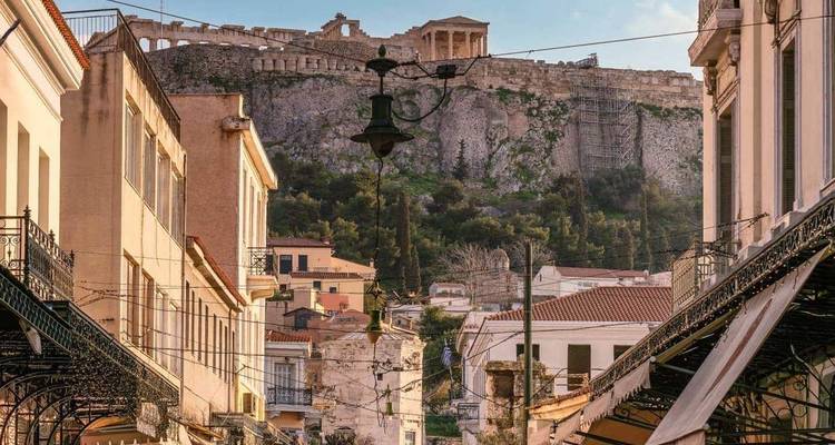 Charming Athens street scene leading up to the illuminated Acropolis and Parthenon at sunset.