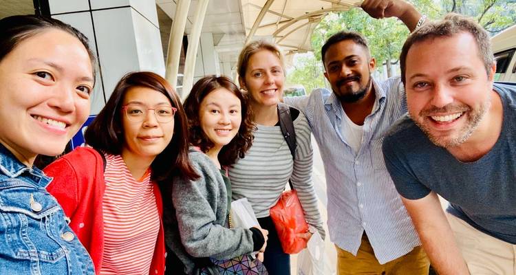 Een groep lachende mensen die poseren voor een selfie in een buitenomgeving.