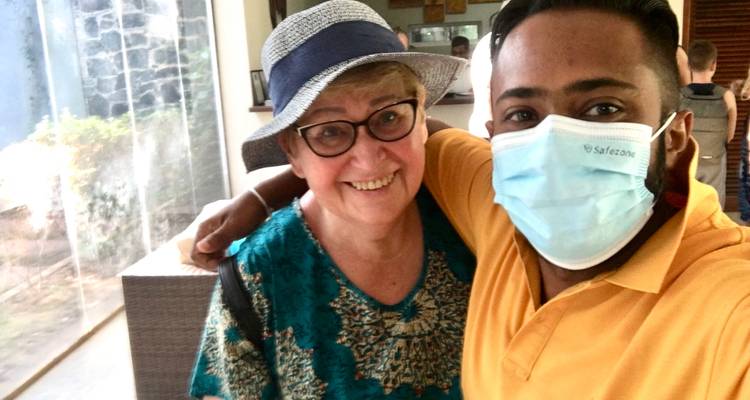 Twee mensen poseren voor een foto binnenshuis, één draagt een hoed en de ander een masker.