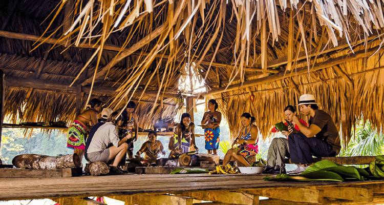 Personas indígenas con ropa tradicional dentro de una cabaña.