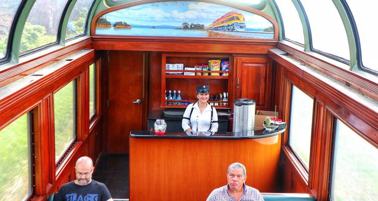 Interior de un vagón de tren con un bar y personas sentadas.