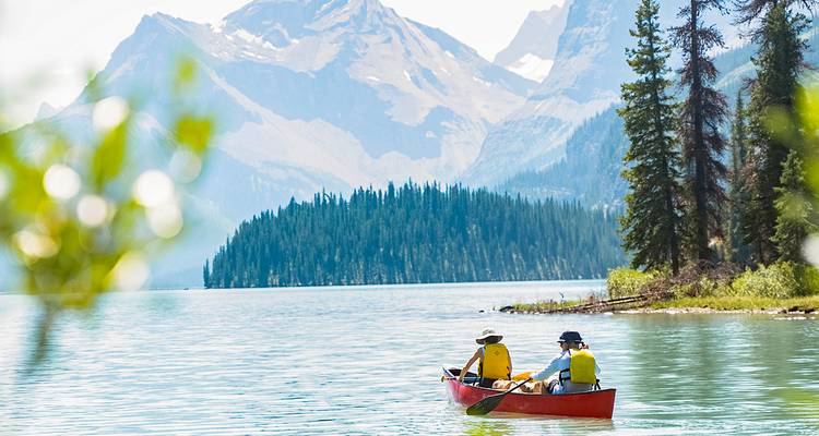 Dos remeros en una canoa roja se deslizan por un lago alpino turquesa rodeado de picos imponentes.