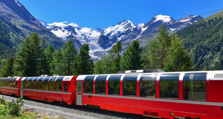 Train rouge traversant un paysage montagneux pittoresque avec des sommets enneigés.