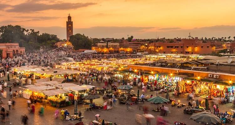 Drukke plein in Marrakesh met kraampjes en mensen tijdens zonsondergang.