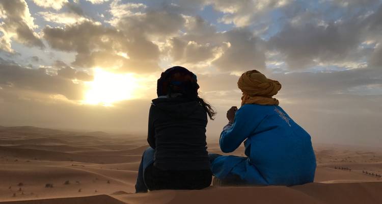 Twee mensen die in de woestijn zitten naar de zonsondergang te kijken.