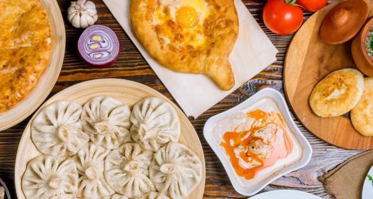 Festin géorgien traditionnel avec boulettes khinkali, khachapuri et assortiment de sauces sur une table rustique.