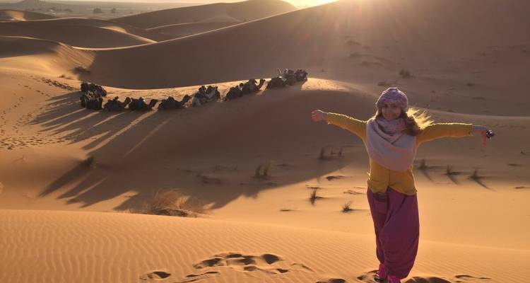 Personne prenant la pose dans le désert avec des chameaux.