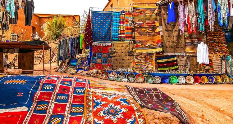 Tissus colorés et tapis suspendus dans un marché marocain.