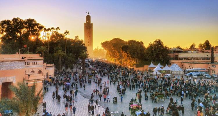 Druk openbaar plein bij zonsondergang met een hoge historische toren.