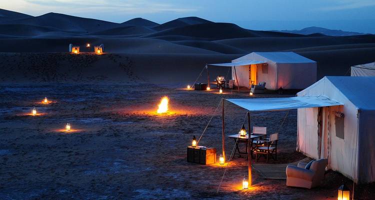 Woestijnkamp 's nachts met kaarsen en een centrale vuurplaats.