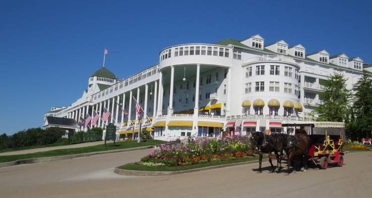 Élégant Grand Hôtel blanc avec des drapeaux américains et une calèche au milieu de parterres de fleurs colorés sur l'île de Mackinac.