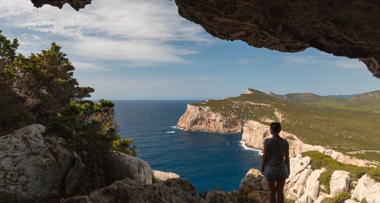 Personne debout à l'entrée d'une grotte surplombant la mer.