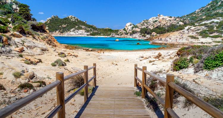 Malerischer Strand mit türkisfarbenem Wasser, Felsen und einem Holzweg, der zum Strand führt.