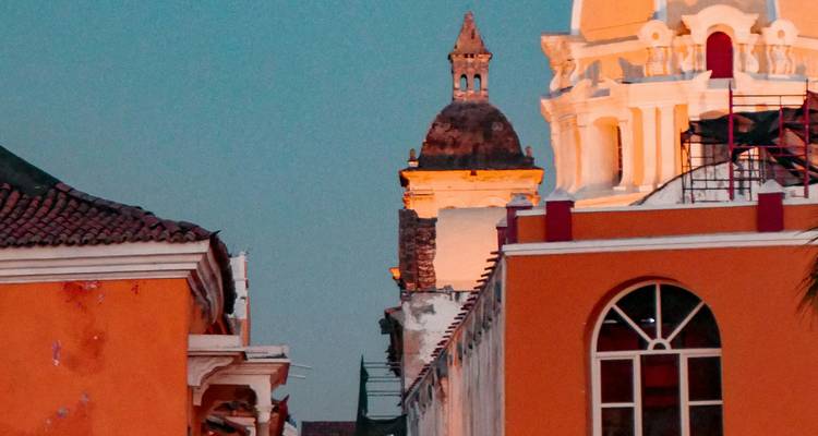 Zacht avondlicht baadt oranje koloniale gevels en een witte kerkentoren die boven de daken uittorent.
