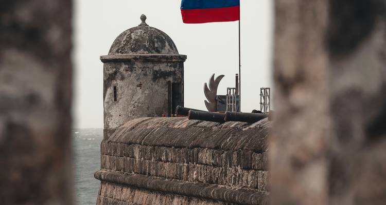 Historische stenen bastei met Colombiaanse vlag die over de zee waakt, omgeven door verweerde muren.