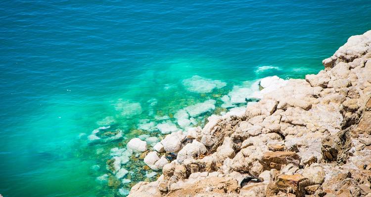 Turquoise wateren van de Dode Zee met rotsformaties aan de oever.