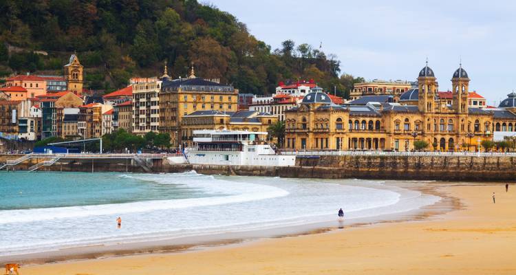 Vista frente al mar con edificios históricos y olas.