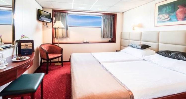 Bright hotel room with a double bed, chair, and large window.