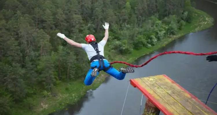 Person bungee jumping over a river with forest surroundings.