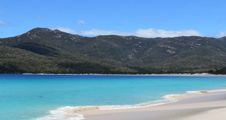 Una playa prístina con agua turquesa y colinas boscosas en el fondo.