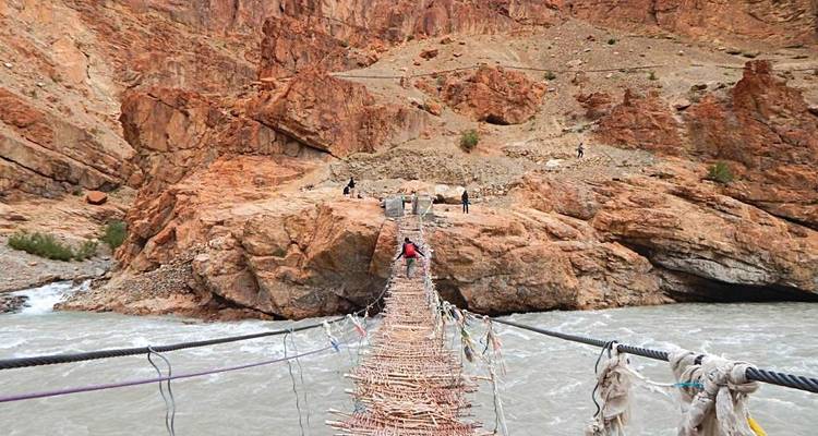 People crossing a deep canyon on a rope bridge.