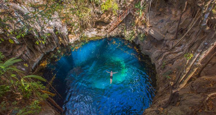 Un nadador solitario flotando en las aguas cristalinas de color azul de un cenote hundido rodeado de rocas.
