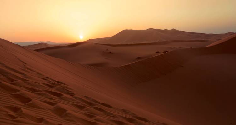 Un coucher de soleil sur des dunes de sable dans un paysage désertique.