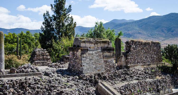 Ruinas de piedra del sitio arqueológico de Mitla con montañas distantes y cielo azul de fondo.