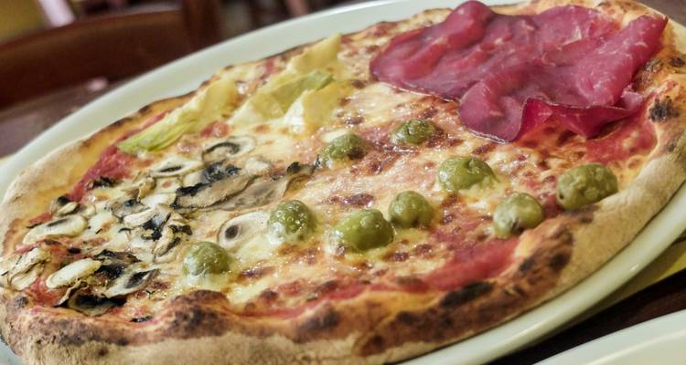 Nahaufnahme einer Holzofenpizza mit verschiedenen Gemüsesorten und Fleischwaren belegt.