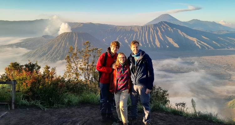 Familia posando en mirador del amanecer con el cráter humeante del Monte Bromo y paisaje volcánico de fondo.