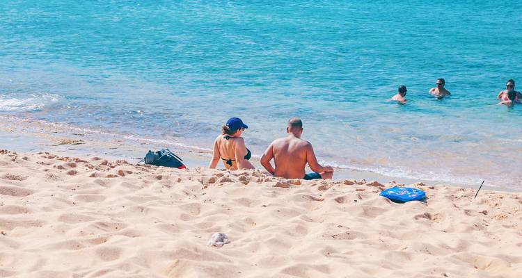 Personas sentadas en una playa de arena mirando hacia el océano.