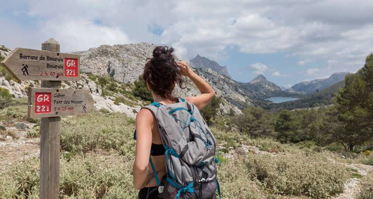 Vue arrière d'une randonneuse étudiant un panneau de sentier GR221 en bois au milieu de pics calcaires escarpés et de végétation arbustive à Majorque.