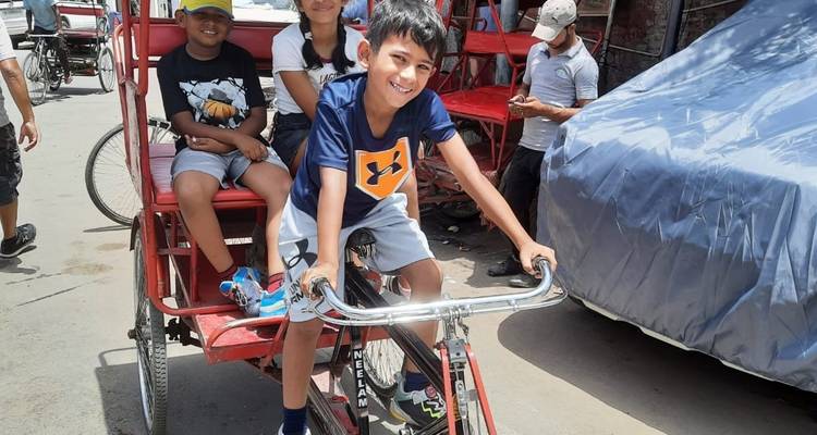 Children riding a bicycle rickshaw in a busy street.