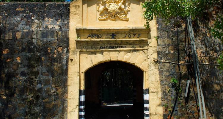 La porte en pierre historique du Fort Frederick datée de 1675 se dresse sous les branches feuillues.