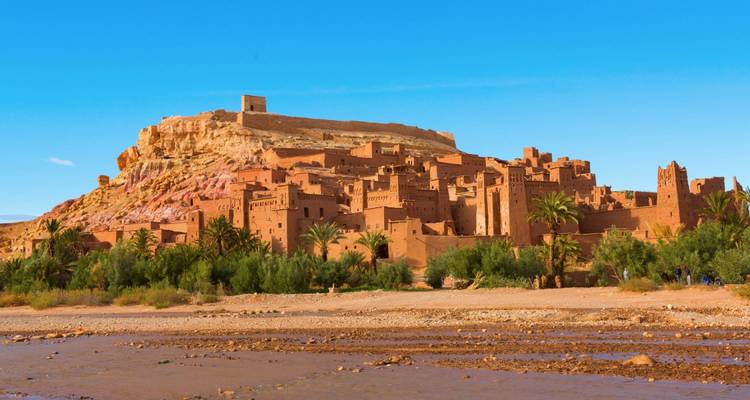 Blick auf das Ksar Ait Benhaddou mit Palmen und blauem Himmel.