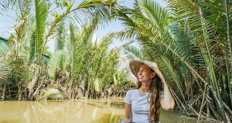 Vrouw glimlachend in een waterweg vol palmbomen.