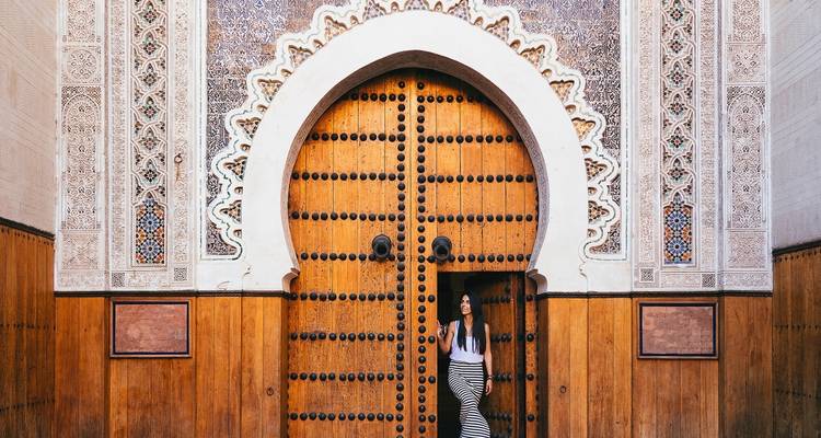 Eine Frau, die vor einer großen, verzierten Tür mit kunstvollen Mustern steht.