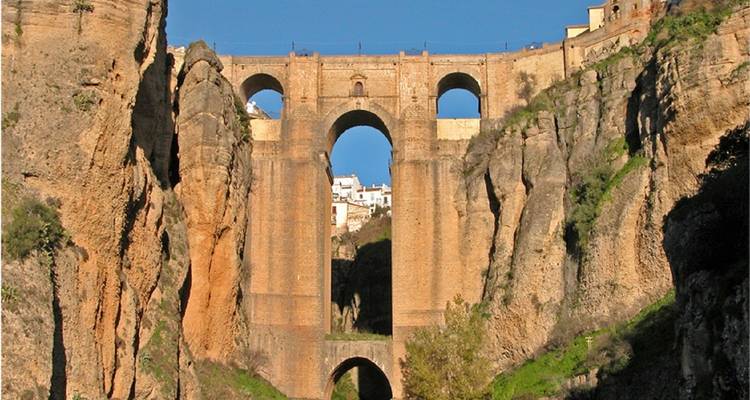 A tall bridge connecting cliffs with a town in the background.