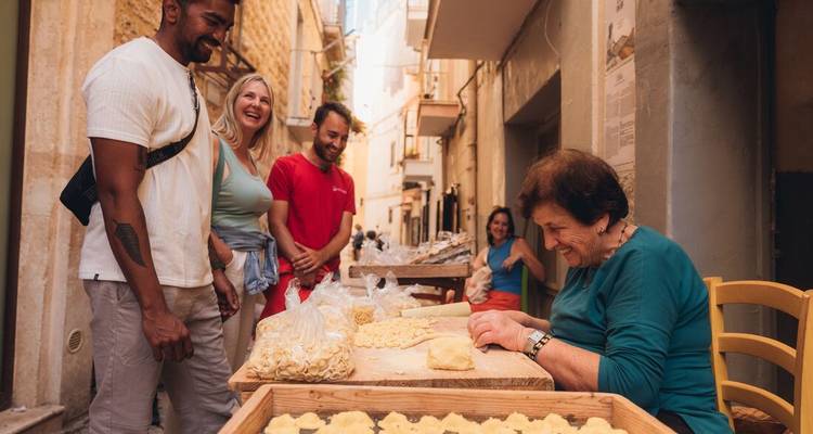 Un groupe de personnes profitant de la préparation traditionnelle de pâtes avec une femme âgée.